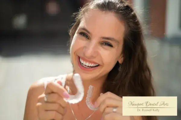 Smiling woman holding aligners at Newport Dental Arts, Dr. Russell Kelly, Newport Beach.